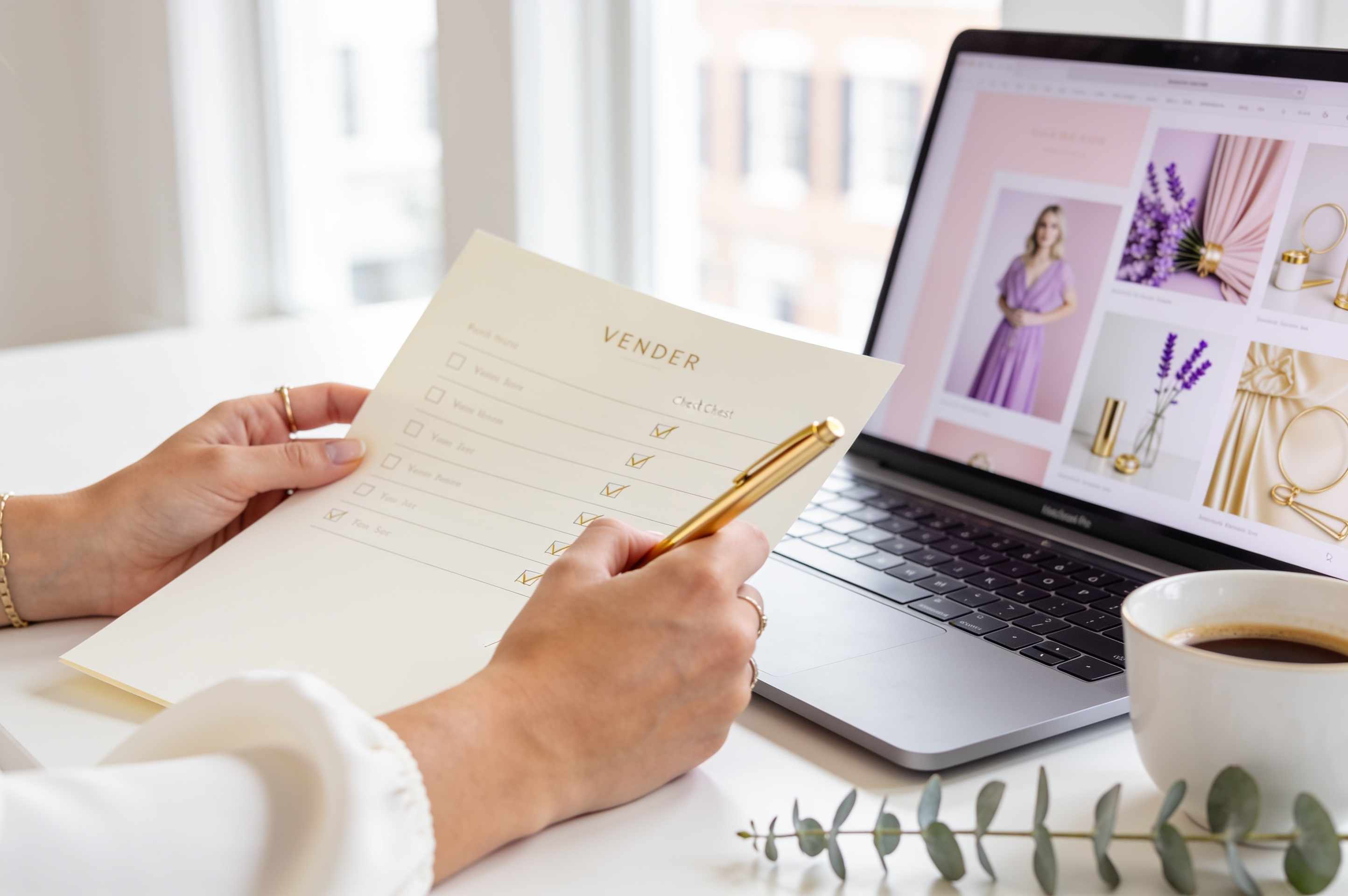 A planner’s hand ticking off a vendor checklist with a gold pen beside a laptop showing a pastel mood board and a sprig of eucalyptus.